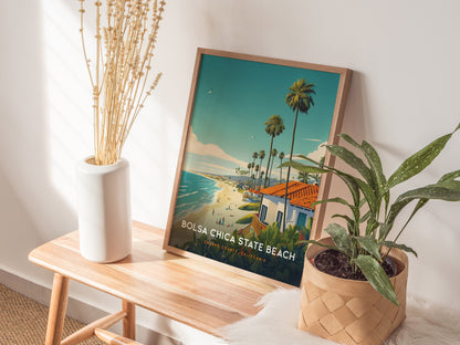 A framed Bolsa Chica State Beach poster rests on a wooden bench, accompanied by a white vase with dried flowers and a potted green plant. Sunlight casts soft shadows.