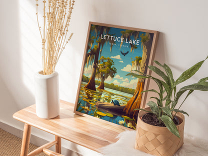 A framed Lettuce Lake Park poster rests on a wooden bench beside a white vase with dried flowers and a potted green plant, creating a serene, nature-inspired decor setting.