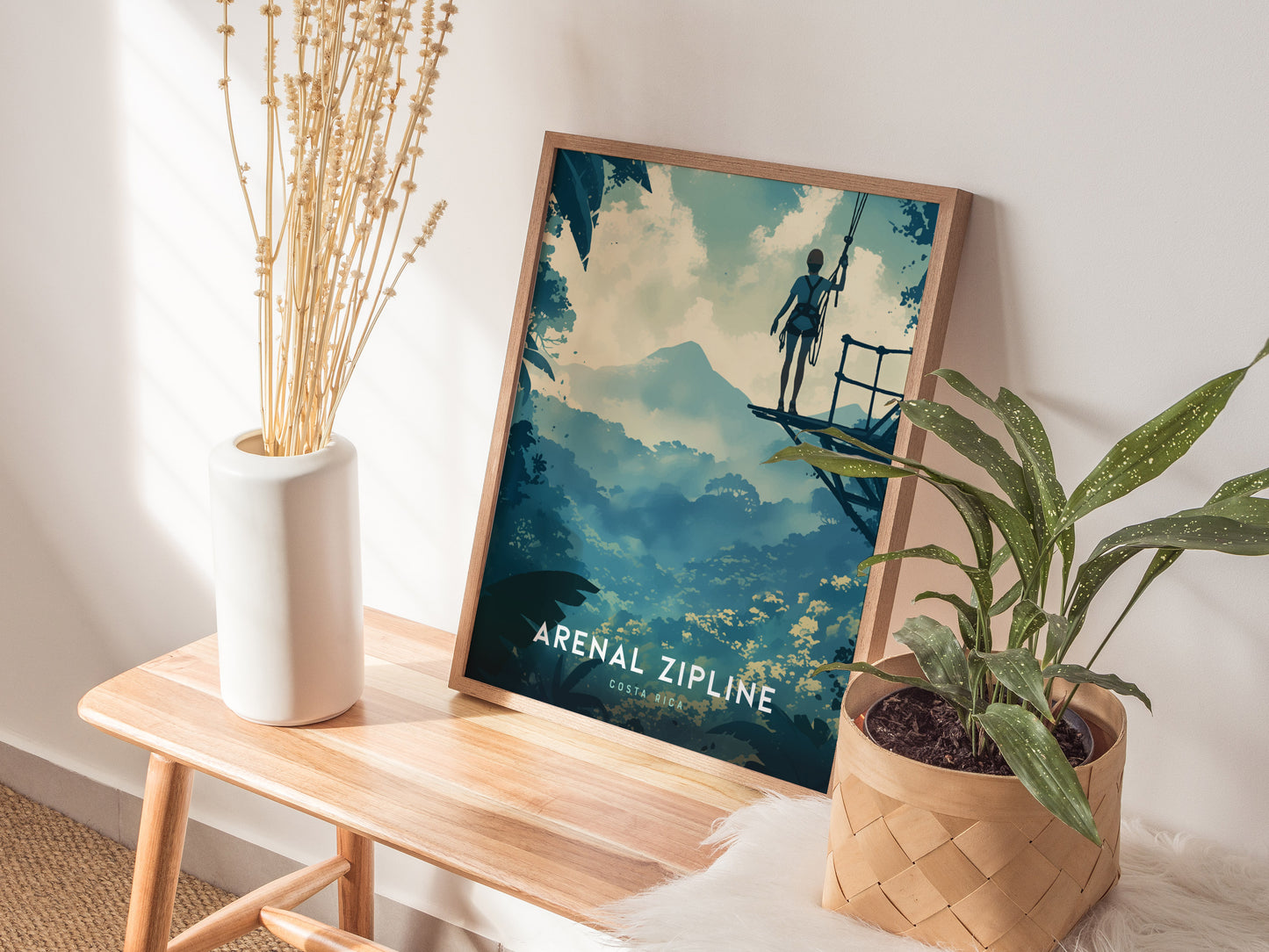 A framed Arenal Zipline Adventure poster rests against a wall, featuring a silhouette on a zipline above a lush forest, with decorative plants in the foreground.