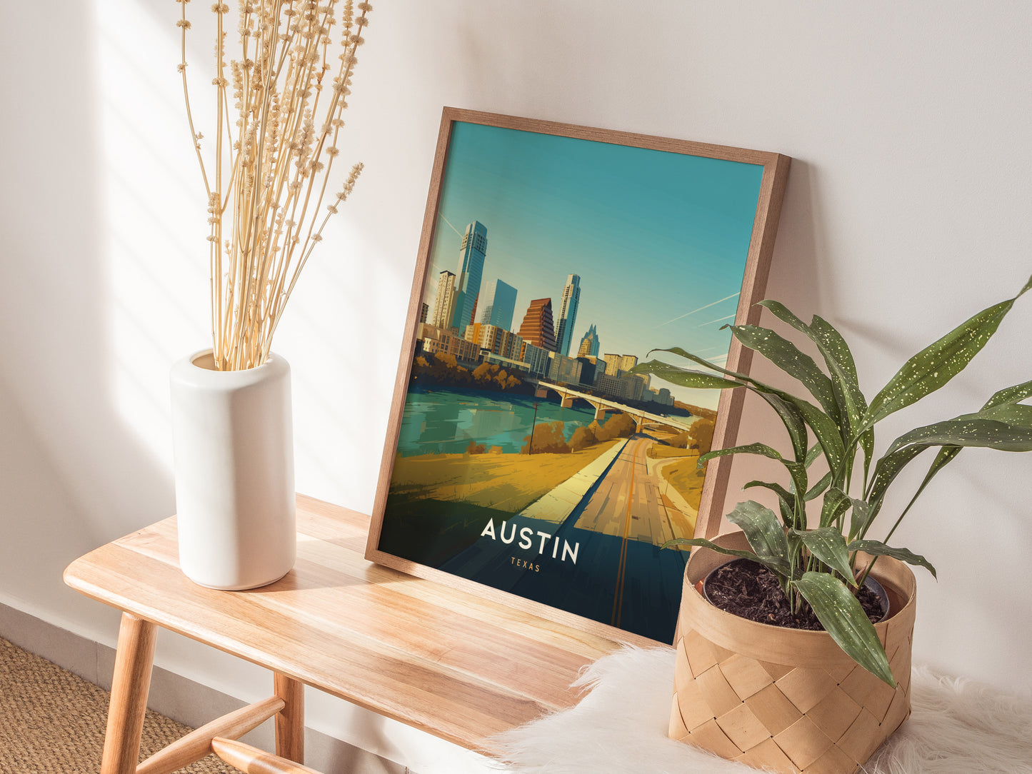 A poster depicting the Austin, Texas skyline rests on a wooden bench, accompanied by a white vase with dried flowers and a green potted plant.