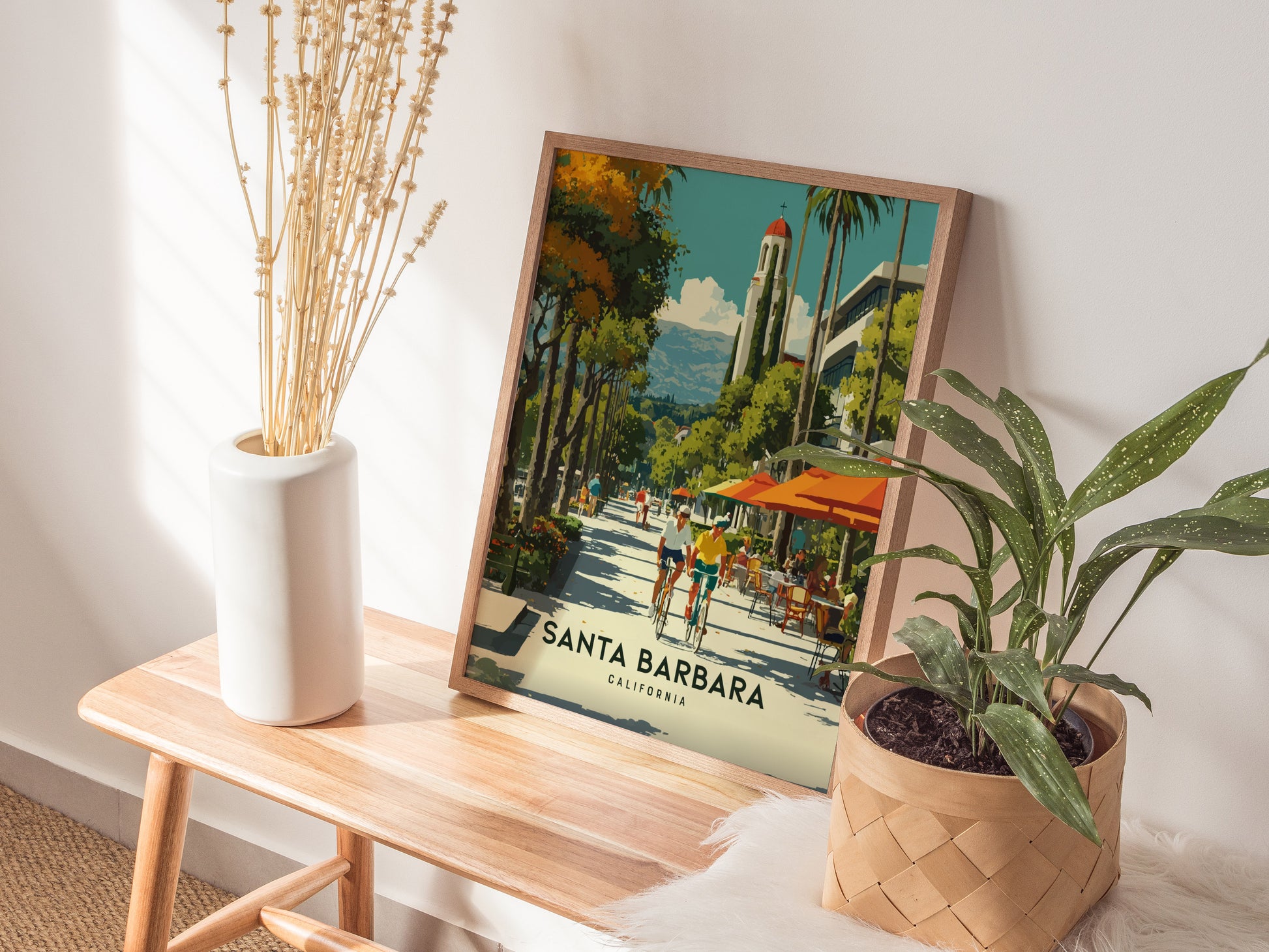 Framed artwork of Santa Barbara on a wooden table with plants and a vase.