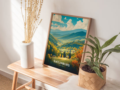A framed Gatlinburg, Tennessee poster featuring colorful mountains and valleys rests on a wooden bench, next to a white vase with dried flowers and a potted plant.