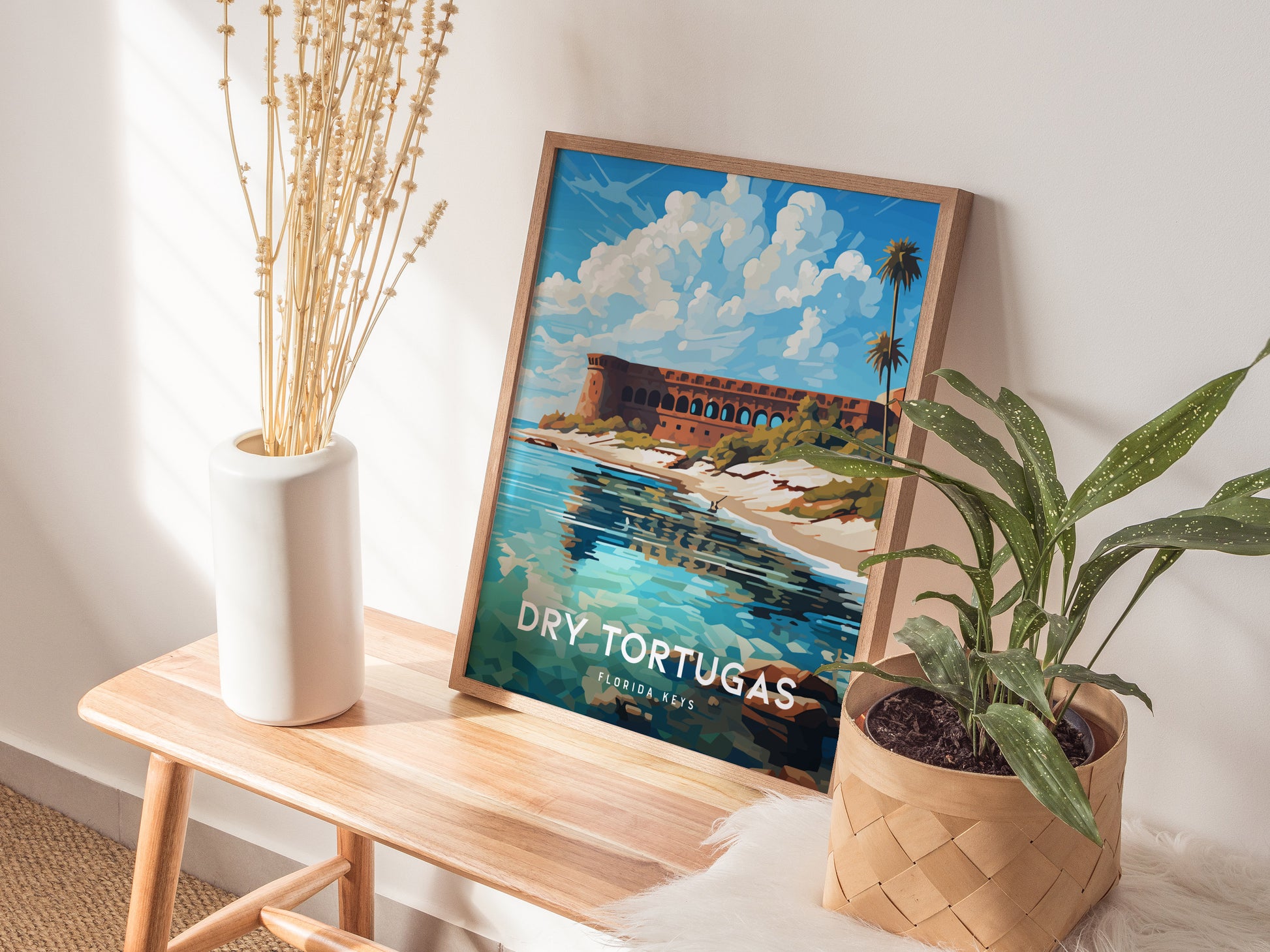 A framed poster of Dry Tortugas National Park, featuring a vibrant illustration of Fort Jefferson by turquoise waters, is displayed on a wooden bench next to plants.