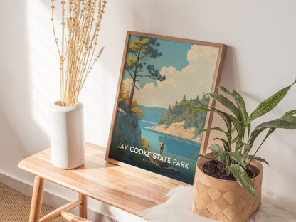 A framed Jay Cooke State Park poster leans against a wall on a wooden bench, accompanied by a white vase with dried flowers and a potted green plant.