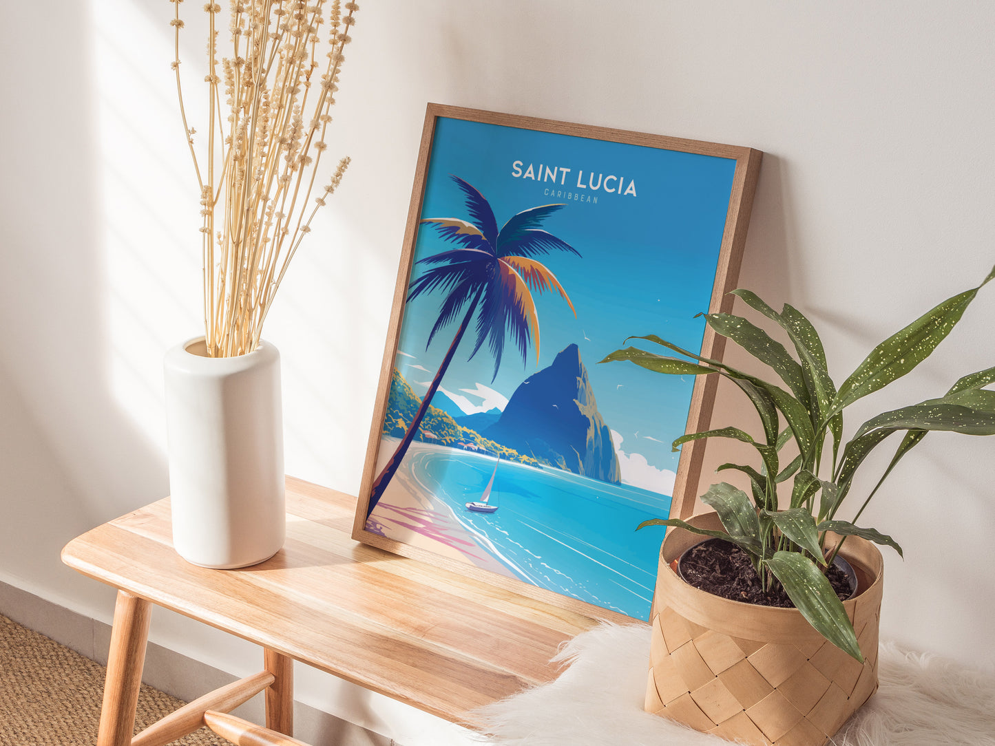 A framed Saint Lucia poster featuring tropical beach art with palm trees and mountains is displayed on a wooden bench beside a white vase and a potted plant.