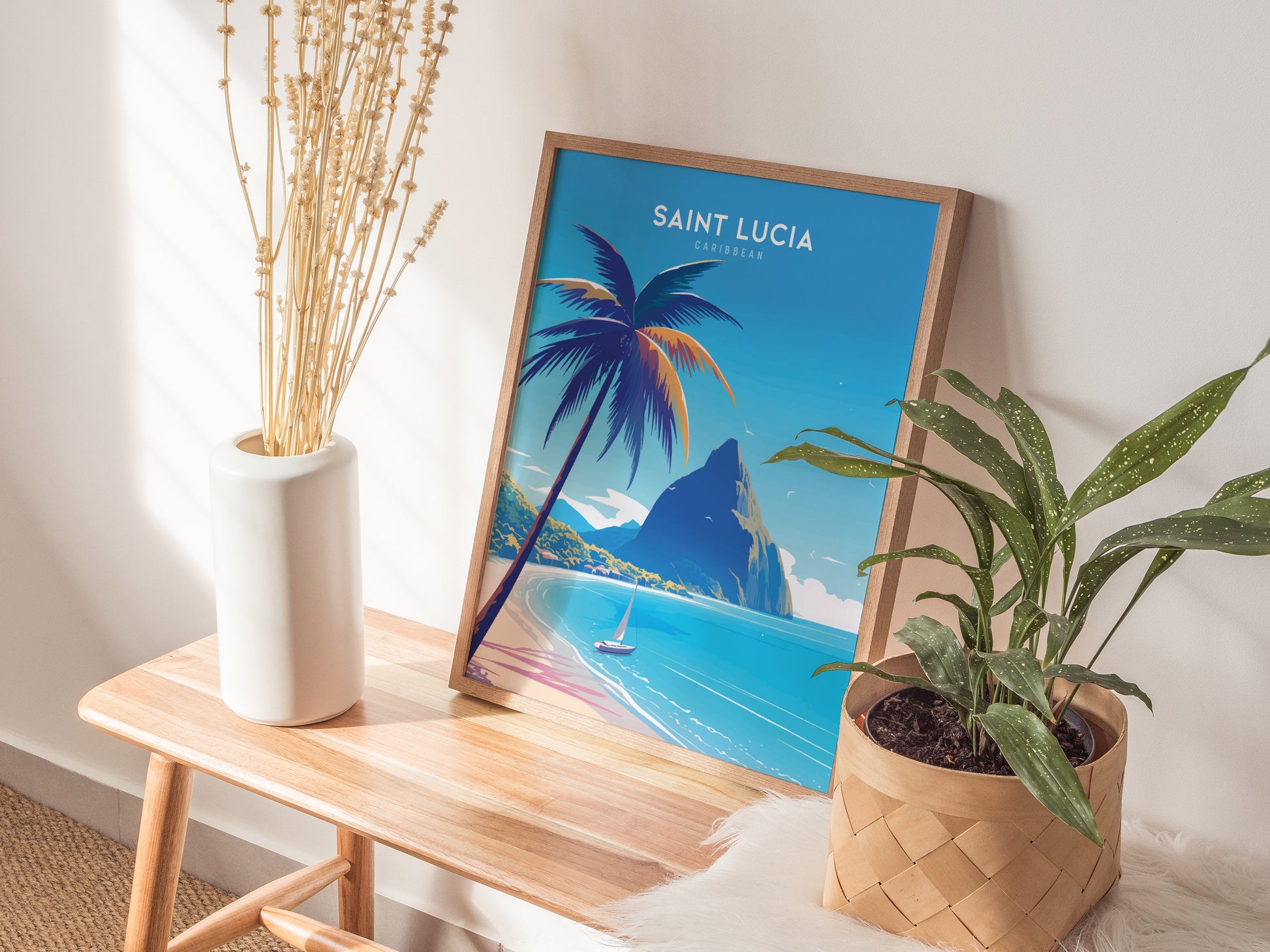 A framed Saint Lucia poster featuring tropical beach art with palm trees and mountains is displayed on a wooden bench beside a white vase and a potted plant.