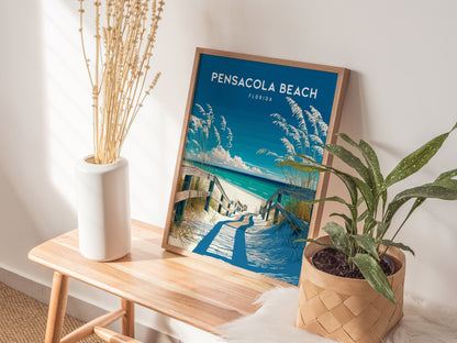A framed Pensacola Beach Florida poster sits on a wooden bench, surrounded by a white vase with dried plants and a potted green plant, creating a coastal decor vibe.