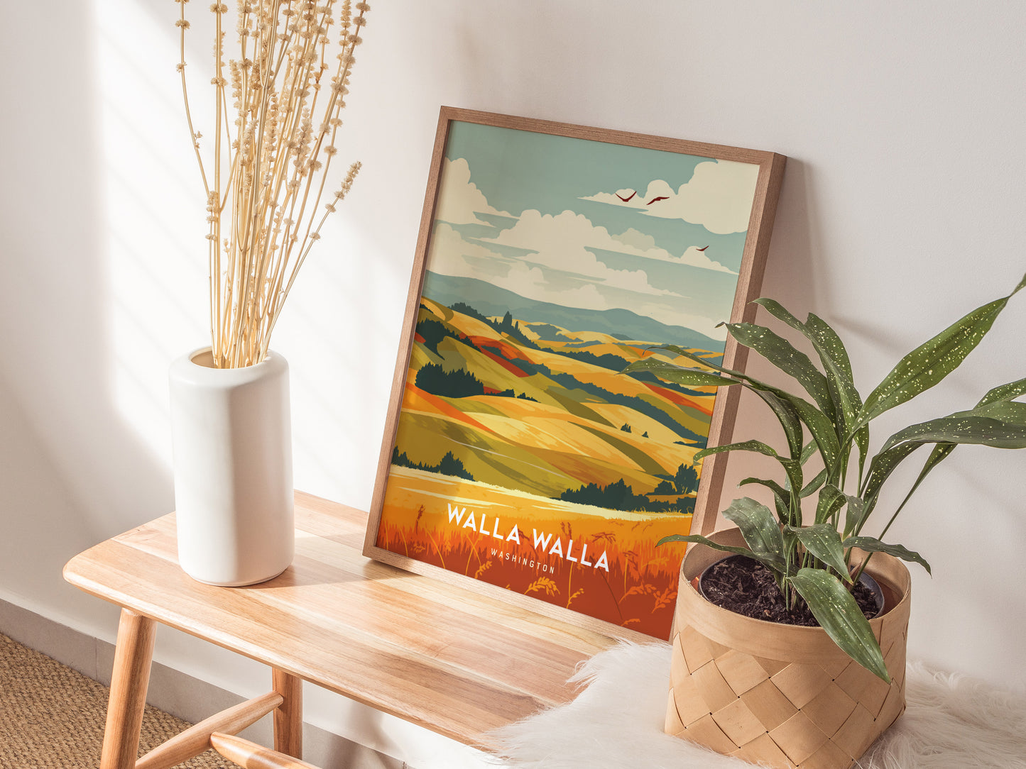 A framed Walla Walla Wineries poster sits on a wooden bench, alongside a white vase with dried stems and a potted plant.