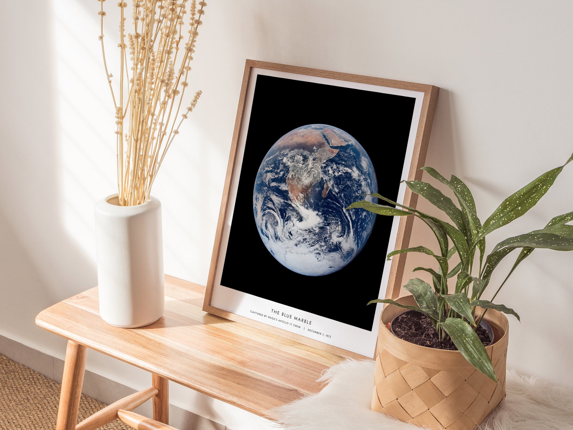 Natural wood framed Blue Marble NASA Earth print leaning on a shelf next to plants and neutral accessories