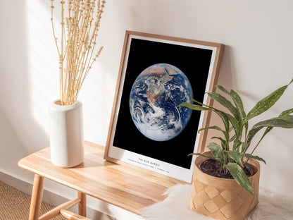 Natural wood framed Blue Marble NASA Earth print leaning on a shelf next to plants and neutral accessories