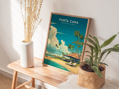A framed Punta Cana poster featuring a tropical beach scene with palm trees and a hut is displayed on a wooden bench. Beside it, a white vase with dried flowers.