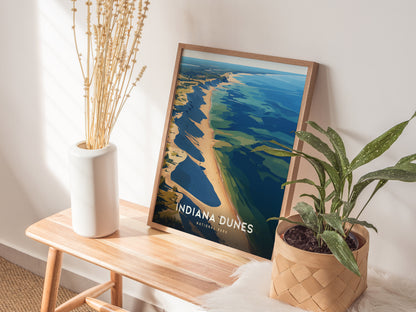 A framed Indiana Dunes National Park poster sits on a wooden bench, accompanied by a white vase with dried flowers and a potted green plant. Natural light casts shadows.