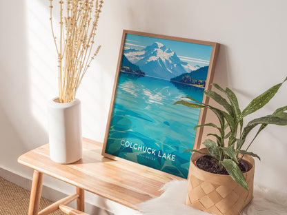 A framed Colchuck Lake poster leans against a wall on a wooden bench, flanked by a white vase with dried stems and a potted green plant.