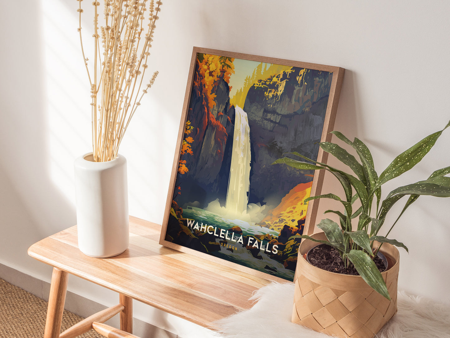 A framed Wahclella Falls poster is displayed on a wooden bench alongside a white vase with dried flowers and a potted green plant, creating a serene decor setting.