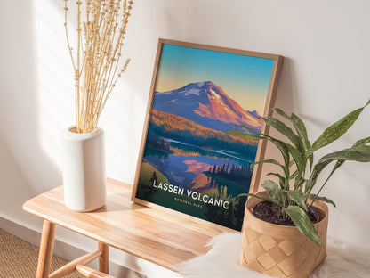 A framed Lassen Volcanic National Park poster leans against a wall, featuring a colorful mountain scene. Its placed on a wooden bench with a potted plant and a white vase.
