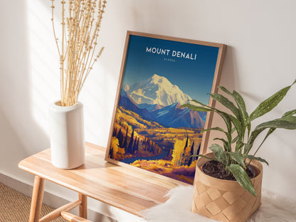 A Mount Denali poster in a wooden frame stands on a wooden bench, accompanied by a white vase with dried flowers and a potted plant in a woven basket.
