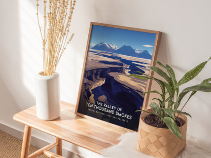 A framed Valley of Ten Thousand Smokes poster leans against a wall on a wooden bench, accompanied by a white vase with dried flowers and a potted plant.