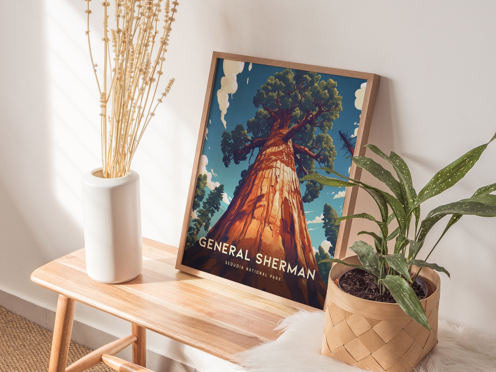 A framed General Sherman poster from Sequoia National Park rests on a wooden table, accompanied by a white vase with dried plants and a potted green plant.
