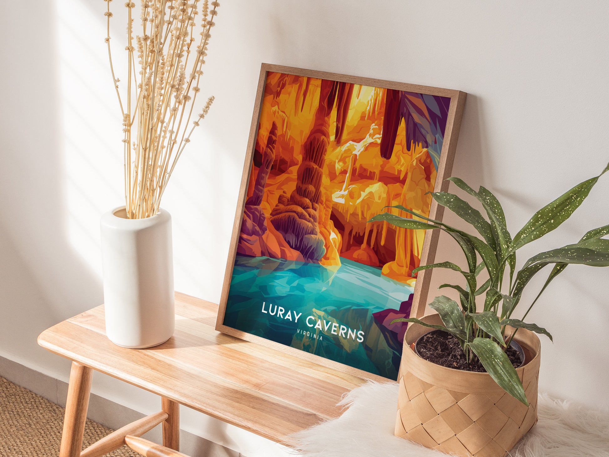 A colorful Luray Caverns poster leans against a wall on a wooden bench, accompanied by a green potted plant and a vase with dried flowers.