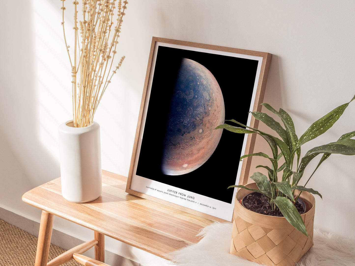 Natural wood framed Jupiter from Juno space print leaning on a shelf next to plants and neutral accessories