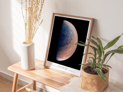 Natural wood framed Jupiter from Juno space print leaning on a shelf next to plants and neutral accessories
