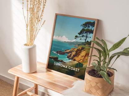 A framed Sonoma Coast poster rests on a wooden bench beside a white vase with dried flowers and a green plant in a woven basket.