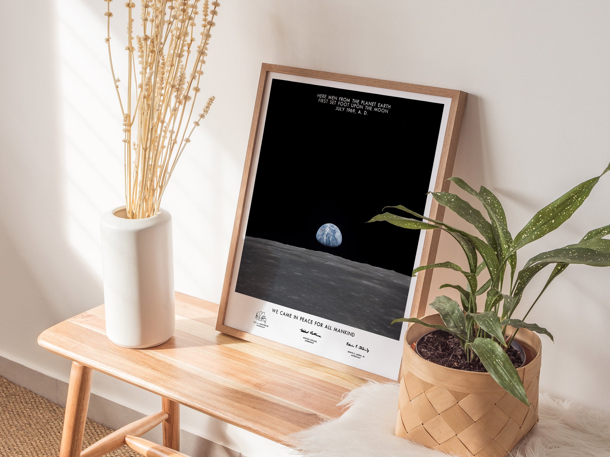 Framed space-themed poster on a wooden side table with plants and a vase.