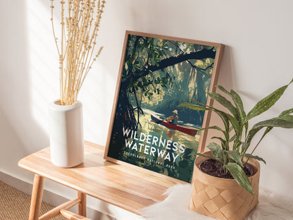 A framed Wilderness Waterway poster rests on a wooden bench beside a white vase with dried flowers and a potted green plant, creating a serene decor setup.