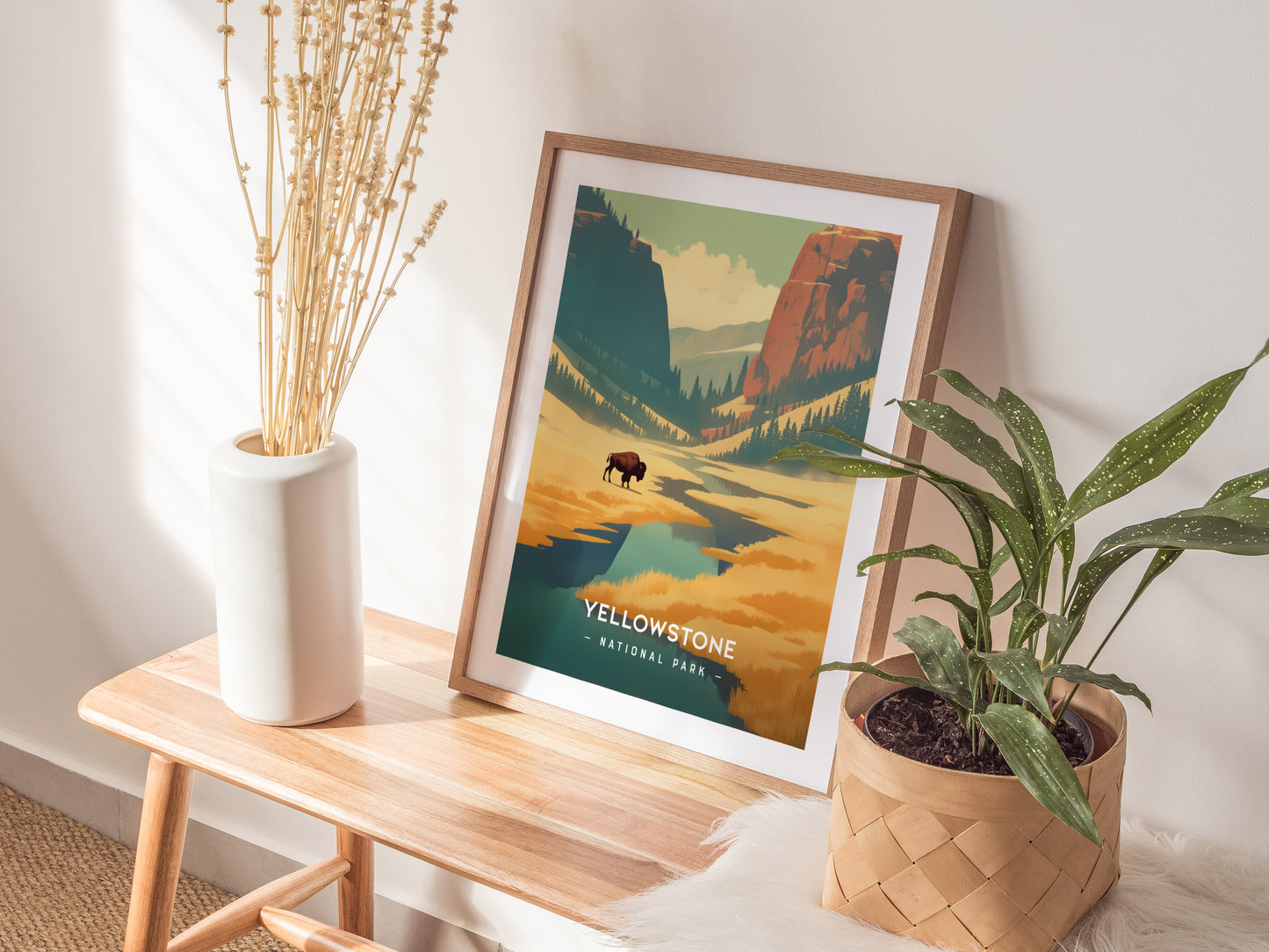 A framed Yellowstone National Park poster with vibrant landscapes is displayed on a wooden bench, accompanied by a white vase with dried plants and a potted green plant.