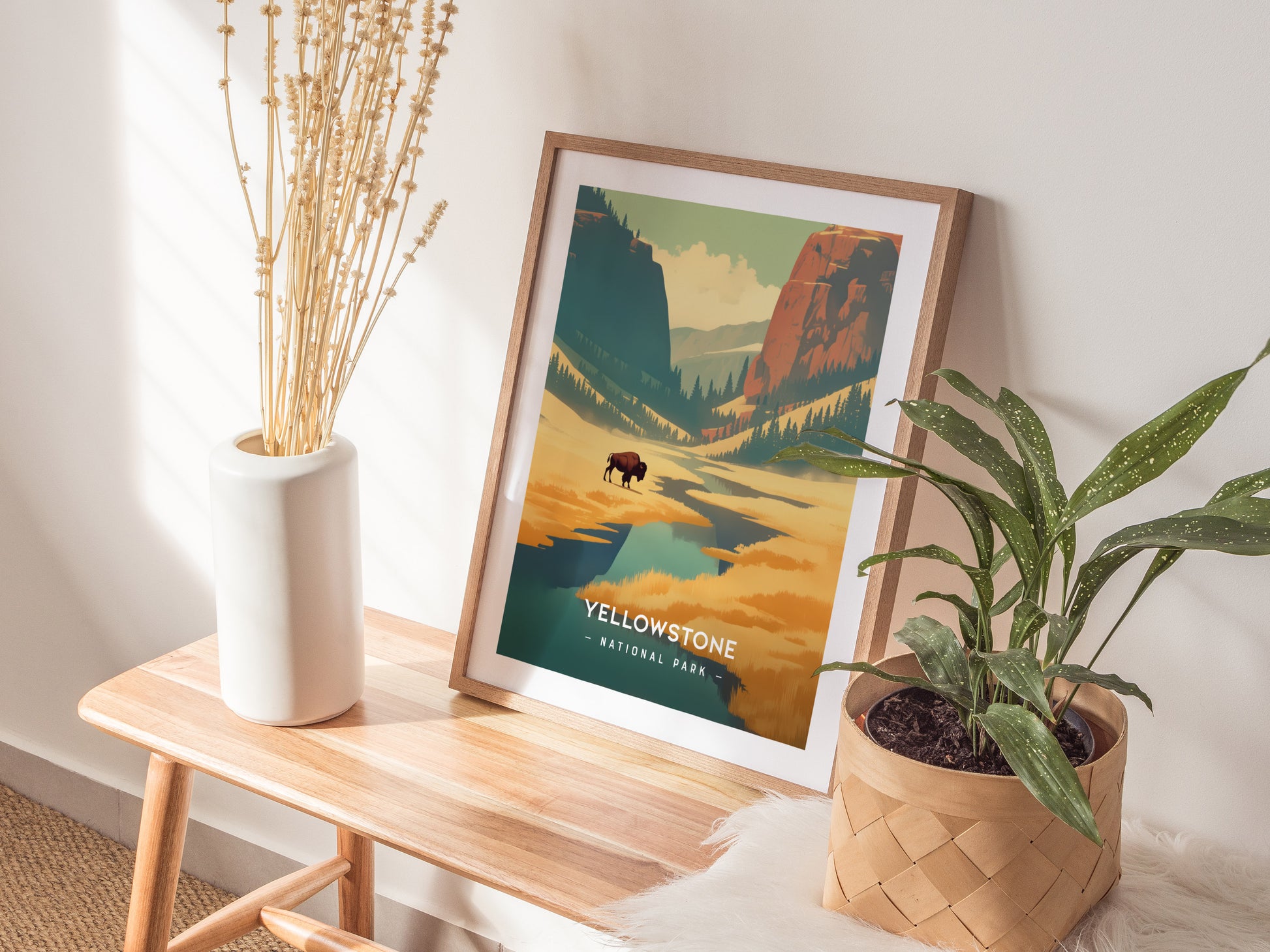 A framed Yellowstone National Park poster with vibrant landscapes is displayed on a wooden bench, accompanied by a white vase with dried plants and a potted green plant.