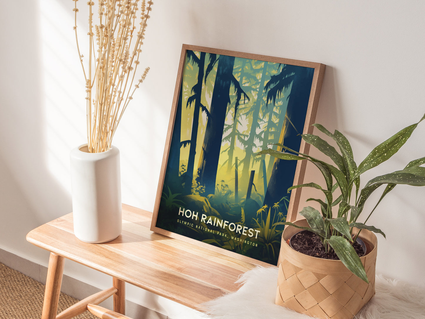 A framed Hoh Rainforest poster leans against a wall on a wooden bench, accompanied by a white vase with dried flowers and a potted plant.