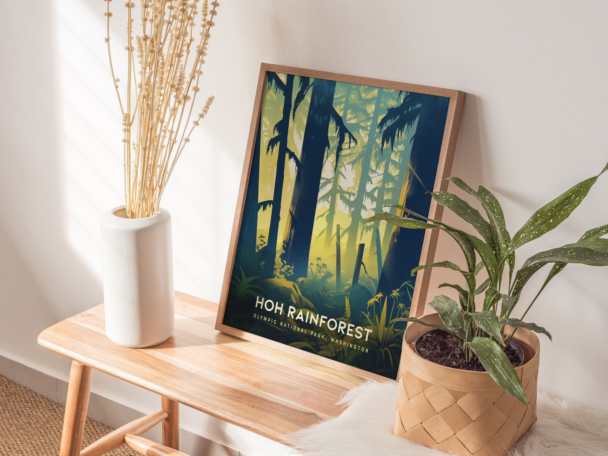 A framed Hoh Rainforest poster leans against a wall on a wooden bench, accompanied by a white vase with dried flowers and a potted plant.