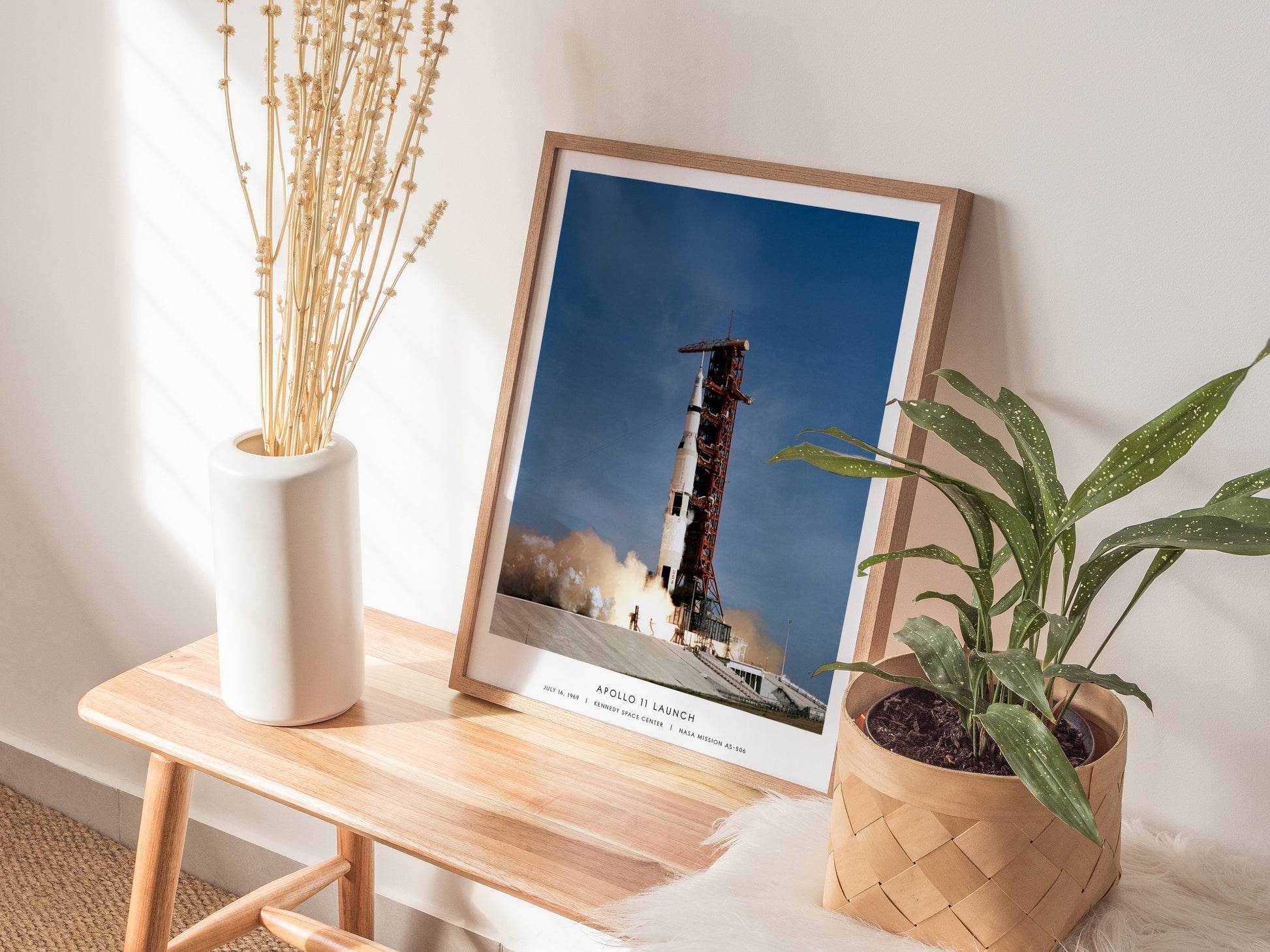 Natural wood framed Apollo 11 launch poster leaning on a shelf next to plants