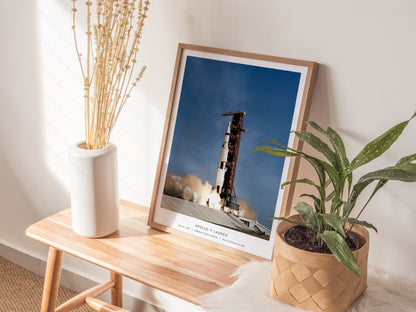 Natural wood framed Apollo 11 launch poster leaning on a shelf next to plants