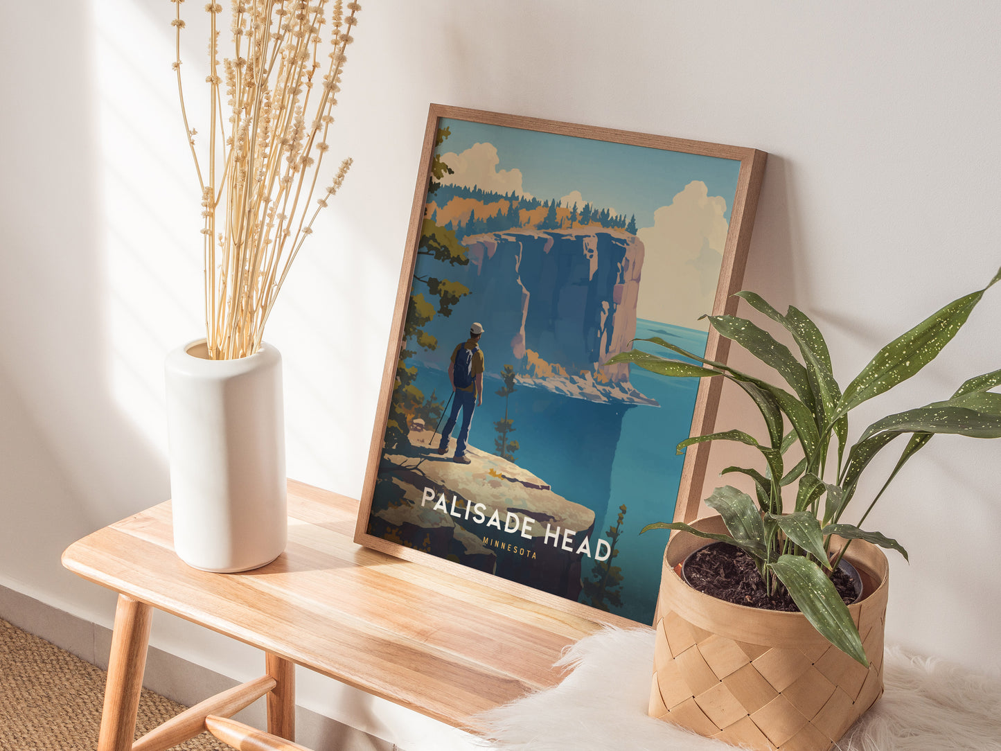 A framed Palisade Head poster is propped against a wall on a wooden bench, accompanied by a white vase with dried flowers and a potted plant.
