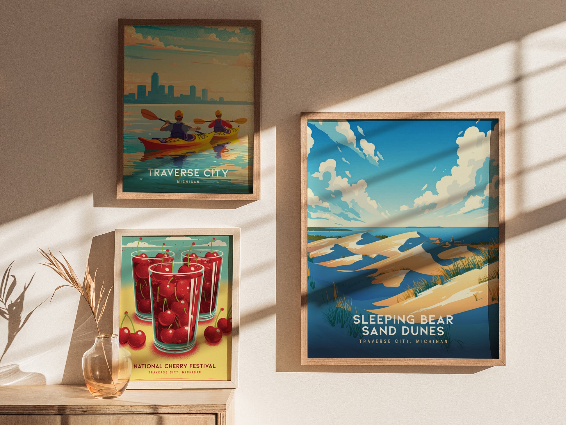 Three framed posters are displayed on a sunlit wall, featuring colorful artwork of Traverse City, Sleeping Bear Sand Dunes, and the National Cherry Festival in Michigan.