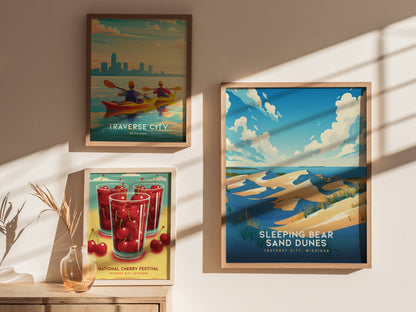 Three framed posters are displayed on a sunlit wall, featuring colorful artwork of Traverse City, Sleeping Bear Sand Dunes, and the National Cherry Festival in Michigan.
