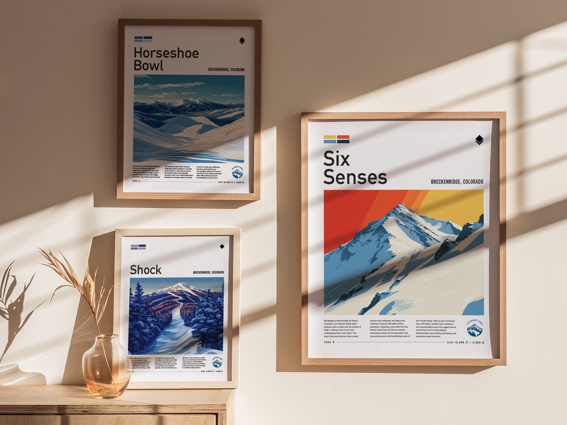 Three framed posters are displayed on a sunlit wall, featuring stylized ski landscapes titled Horseshoe Bowl, Shock, and Six Senses, with vibrant colors and mountain imagery.