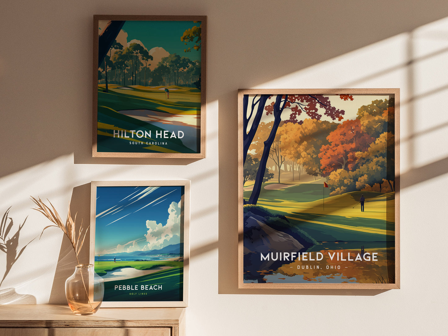 Three framed golf course posters hang on a wall, depicting Hilton Head, Muirfield Village, and Pebble Beach. Sunlight casts shadows, adding warmth to the display.