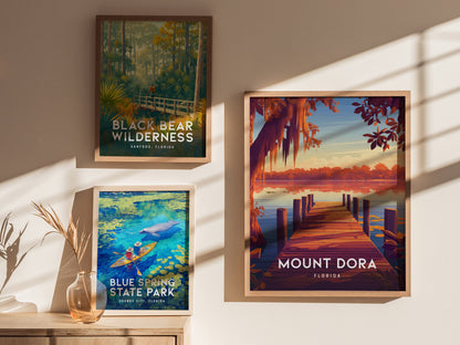 Three framed posters on a wall display scenic Florida locations: Black Bear Wilderness, Blue Spring State Park with a kayaker, and Mount Dora featuring a sunset over a lake.