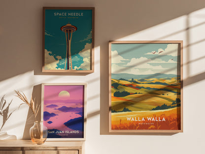 Three framed posters are displayed on a sunlit wall, featuring the Space Needle, San Juan Islands, and Walla Walla landscapes, with soft shadows and a vase of dried plants nearby.