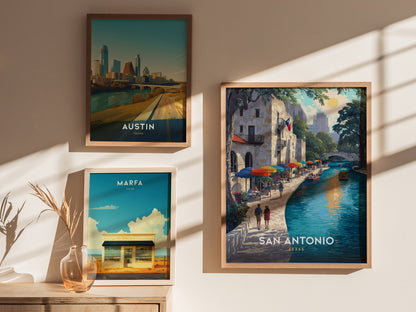 Three framed posters hang on a wall, depicting Austin, Marfa, and San Antonio. The San Antonio poster features a vibrant riverside scene with colorful umbrellas and a serene waterway.