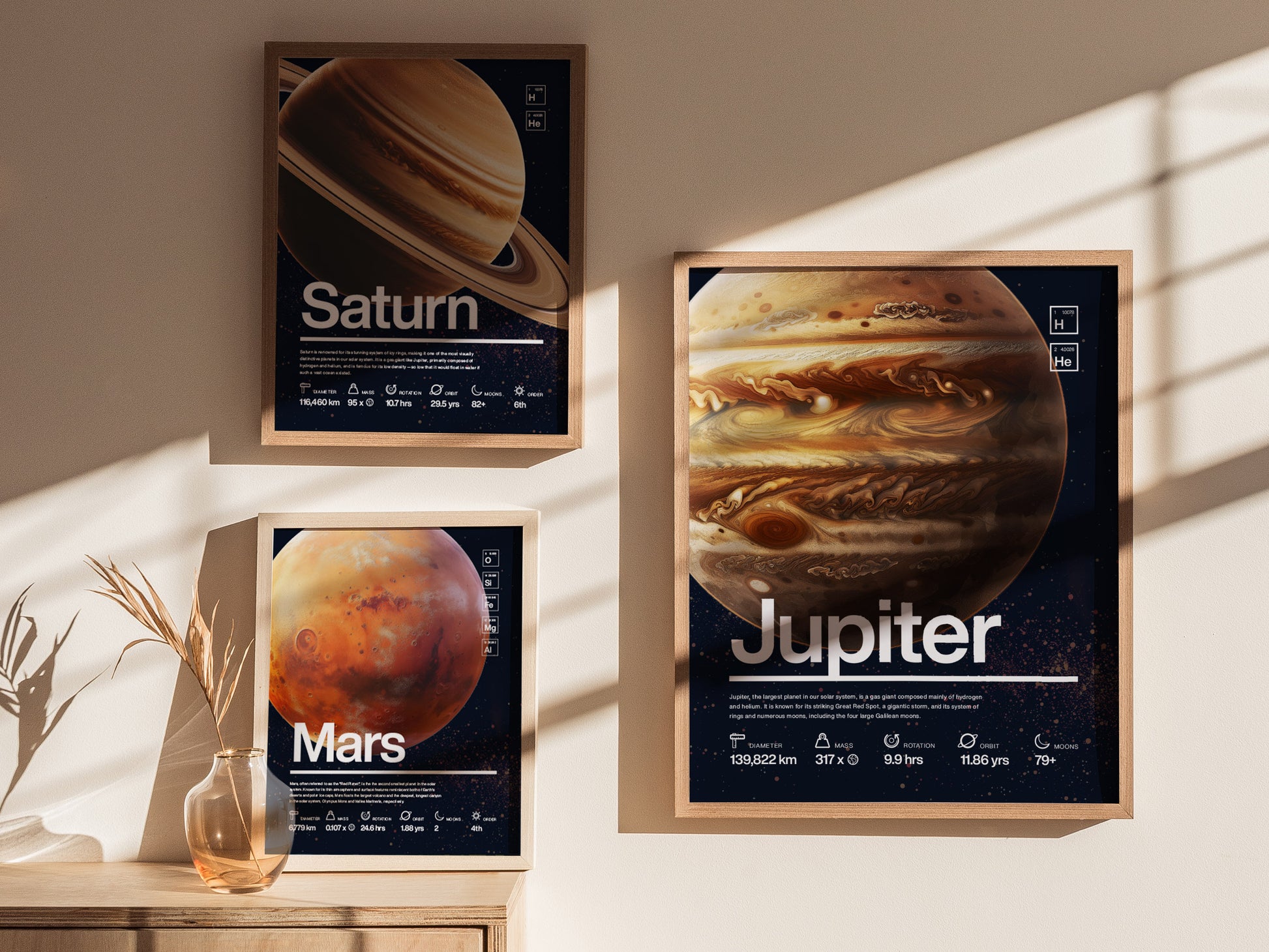Three framed posters of planets Saturn, Jupiter, and Mars are displayed on a sunlit wall, with a small vase of dried plants on a wooden surface below.