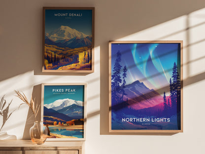 Three framed posters are displayed on a wall. They depict Mount Denali, Pikes Peak, and the Northern Lights over a mountainous landscape, with sunlight casting shadows across them.