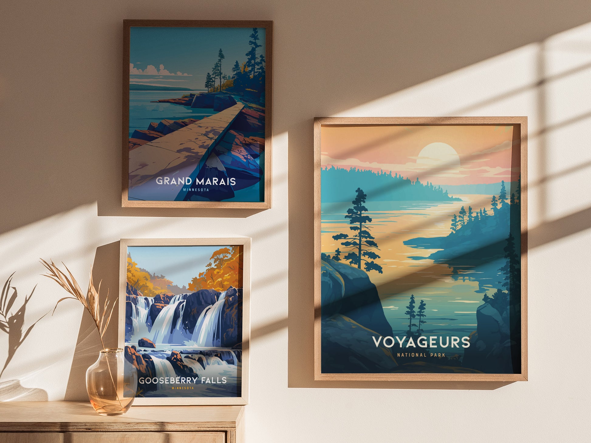 Three framed posters are displayed on a sunlit wall, featuring Grand Marais, Gooseberry Falls, and Voyageurs National Park, each depicting scenic landscapes with water and trees.