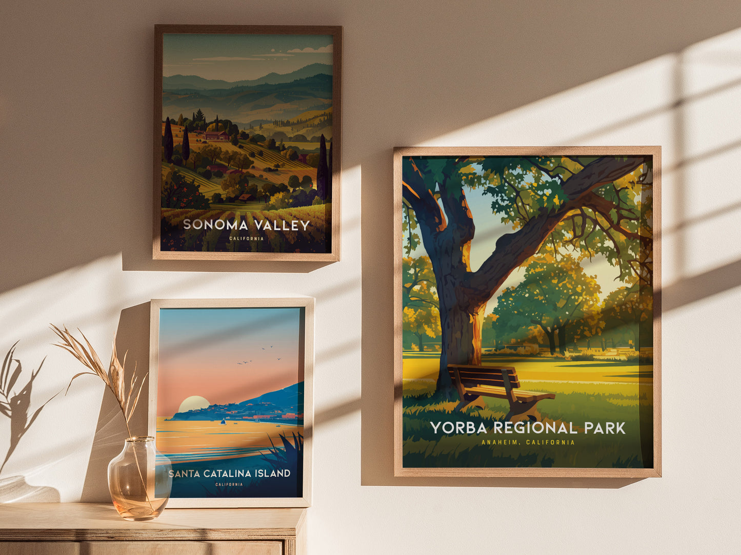 Three framed posters hang on a sunlit wall, featuring Sonoma Valley, Santa Catalina Island, and Yorba Regional Park, each with vibrant landscapes and distinct natural elements.
