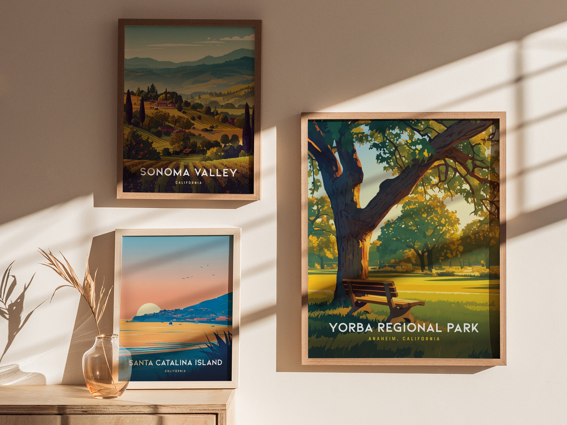 Three framed posters hang on a sunlit wall, featuring Sonoma Valley, Santa Catalina Island, and Yorba Regional Park, each with vibrant landscapes and distinct natural elements.