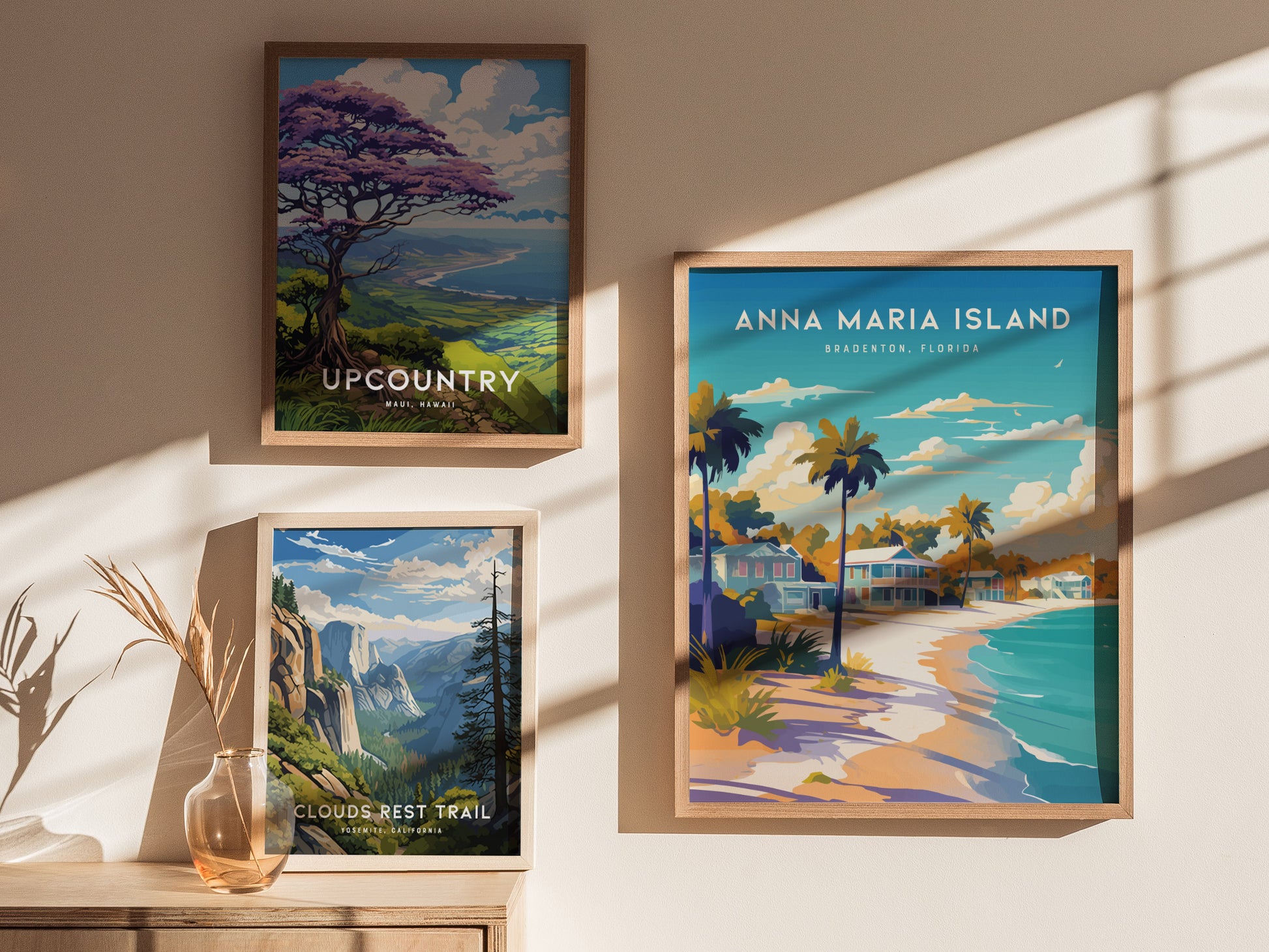 Three framed art prints are displayed on a sunlit wall. The largest features a coastal scene titled Anna Maria Island, Bradenton, Florida with colorful beach cottages and palm trees.