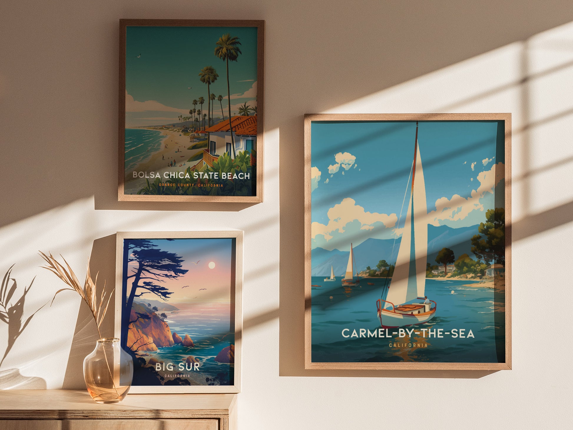 Three framed coastal art prints are displayed on a wall, featuring scenes from Carmel-by-the-Sea, Bolsa Chica State Beach, and Big Sur, with natural light casting shadows.