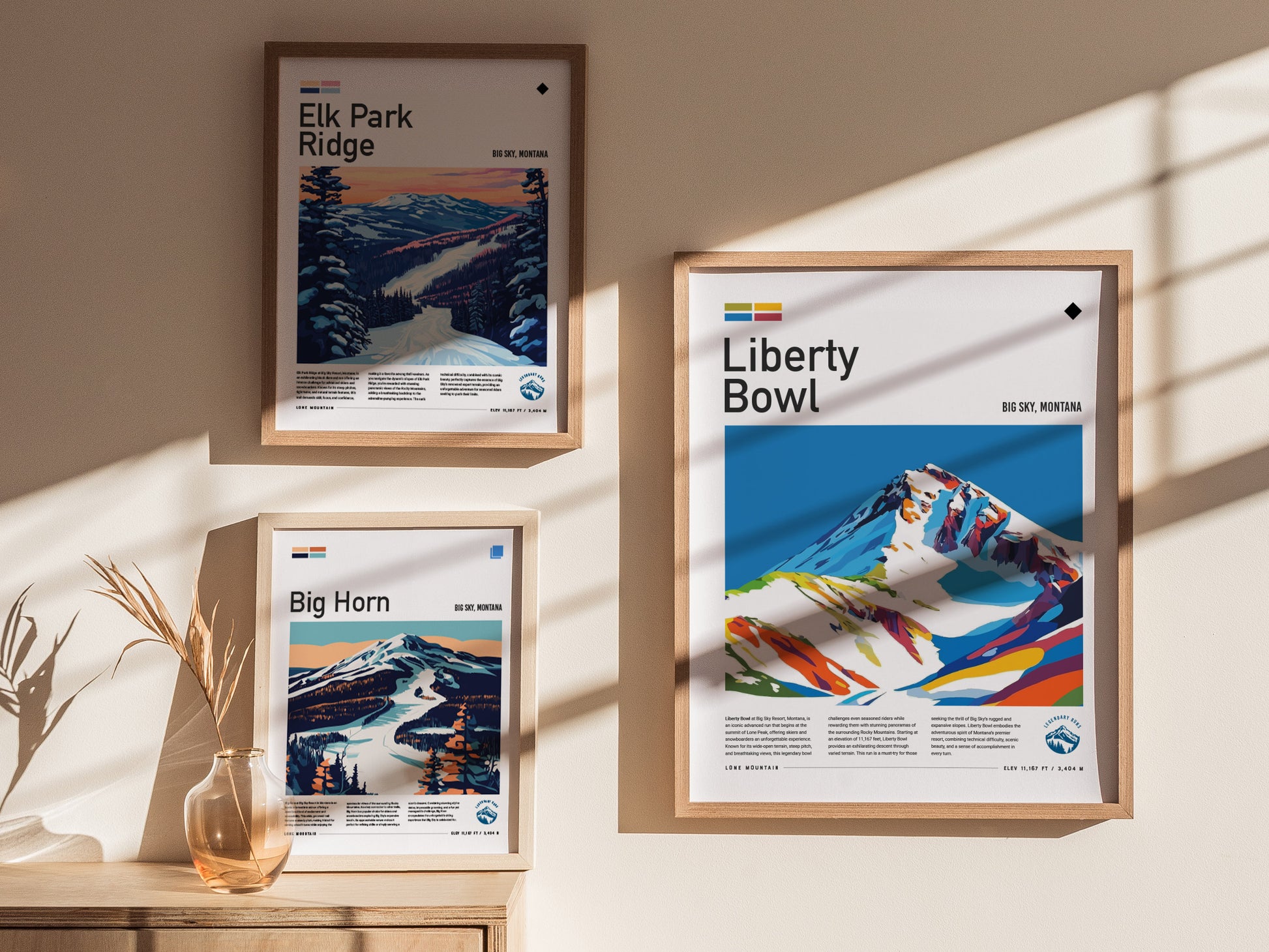 Three framed posters are hung on a wall, depicting colorful mountain scenes labeled Elk Park Ridge, Liberty Bowl, and Big Horn. Sunlight casts shadows across the posters.